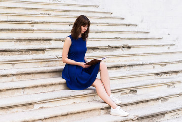 girl in blue dress sitting on the steps and reading a book