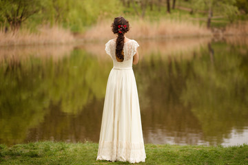 Rear view of a young anonymous bride in a beautiful full wedding dress, with hairstyle, looking down, nature background.