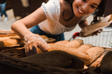 cropped view of happy woman in glove near bread in supermarket