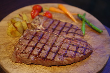 Grilled t bone steak with potato, carrot, cherry tomato and asparagus on round wooden tray