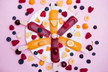 Helados veganos hechos con fruta natural en un plato sobre un fondo rosa pastel y frambuesas, arándanos, cerezas, piña, plátano, melocotón y melón.