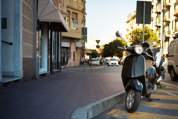 Black classic scooter with a chrome round headlight in the urban environment of Italy