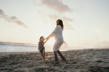 Fototapeta na wymiar young beautiful pregnant woman with her little cute daughter playing in the beach when sunset time in the evening