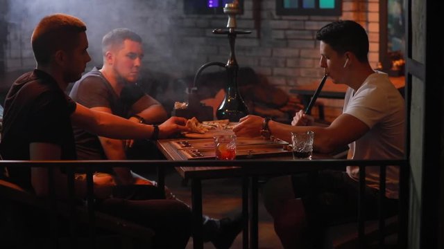 Men friends smoking hookah playing backgammon in a bar