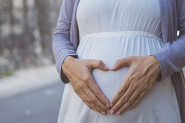 gesture of heart shape on pregnant belly.Outdoor background