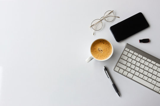 business concept. top view of office desk workspace with smartphone, pen, keyboard, glasses and hot coffee cup on white table background. over light