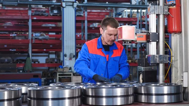 Male worker in blue uniform in bearing factory. Mechanic assembles bearings , Industry concept. A qualified employee at plant putiing large bearings under laser marking machine. close-up, 4k
