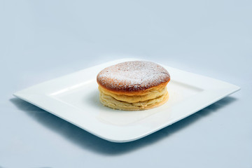 A low contrast Hero Shot of a pan cake on a plate, on a minimal white background with a diagonal 60 degree angle