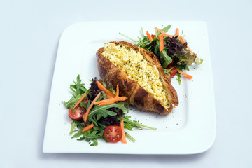 A low contrast image of a breakfast platter with egg-filled croissant with vegetables- carrot, tomato, lettuce on a minimal white background with a 30 degree angle from front perspective