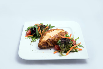 A low contrast image of a breakfast platter with cheese-filled croissant with vegetables- carrot, tomato, lettuce on a minimal white background with a 30 degree angle from front zoomed in perspective