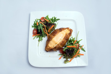 A low contrast image of a breakfast platter with cheese-filled croissant with vegetables- carrot, tomato, lettuce on a minimal white background with a 30 degree angle from front zoomed in perspective