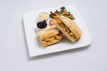 A low contrast Hero shot of a breakfast platter with grilled chicken panini sandwich with olives, cheese & vegetables on a minimal white background with a 45 degree angle from almost front perspective