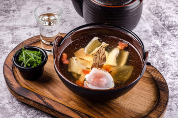 Top view close up Russian traditional fish soup in a bowl - ukha, served with green onions and vodka on on wooden board background. Fish broth in a teapot. traditional cuisine in Russia.