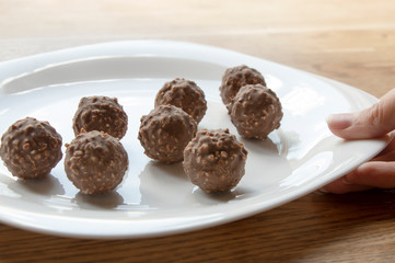 female hand tries round chocolate candy with nuts on a white plate