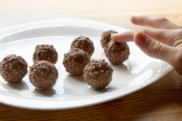female hand tries round chocolate candy with nuts on a white plate