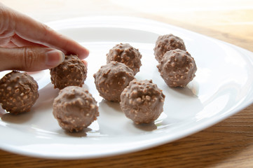 female hand tries round chocolate candy with nuts on a white plate