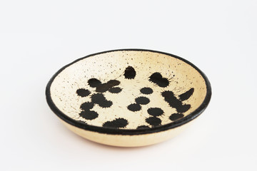 beige clay plate with black spots. made of layer, covered with transparent glaze. two roasting. Handmade ceramics. On a white background.