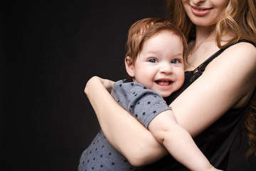 Close-up of cute baby boy smiling at camera while mother is holding him on her loving arms.