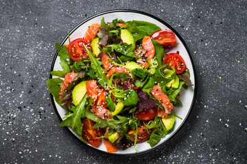 Salmon salad with fresh vegetables on black top view.