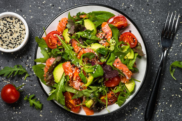 Salmon salad with fresh vegetables on black top view.