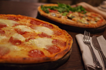 Salami pizza with buffalo cheese and seafood pizza with shrimp, squid, clam and lettuce topping on round wood tray with knife and fork on white napkin