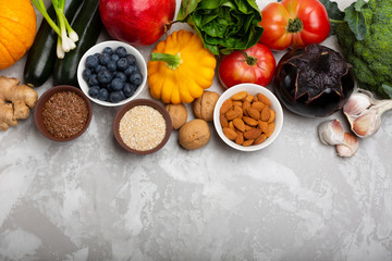 Mix of fresh healthy vegetarian ingredients of vegetables, nuts, seeds, bran, fruit and berries on a gray cement background. Top view, copy space.