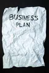 Phrase "business plan" handwritten on crumpled torn paper, top view. Sign, concept of failed plans or poor management, abstract illustrative image