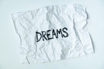 Word "dreams" handwritten on crumpled paper, top view. Sign, concept of broken or failed dreams, abstract illustrative image