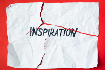 Word "inspiration" handwritten on torn and crumpled paper. Sign, concept of failed plans or hopes, abstract illustrative image in bright red background