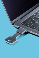 USB-drive in the form of a key through the adapter connected to a modern laptop on a blue background. Vertical.