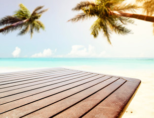 A wooden table background in the beautiful ocean and sunny beach view with palm leaves above. Empty space for an advertising product.