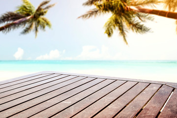 A wooden table background in the beautiful ocean and sunny beach view with palm leaves above. Empty space for an advertising product.
