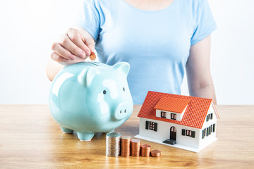 Housewife saves money to buy a house, female hand takes a coin into a piggy bank and a small house...