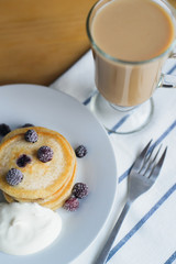 circular oladyi or pancakes with black raspberry on white plate with smetana and coffee on wooden table, eastern europe breakfast, close up view from above of vertical still life stock photo image