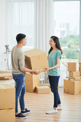 Young Asian family carrying packed cardboard box together while moving in their new apartment