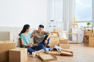 Fototapeta na wymiar Young Asian couple sitting on the floor eating pizza together they resting after moving in new apartment