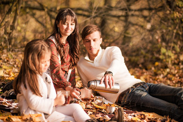 Family picnic in the autumn park. Family drinking tea