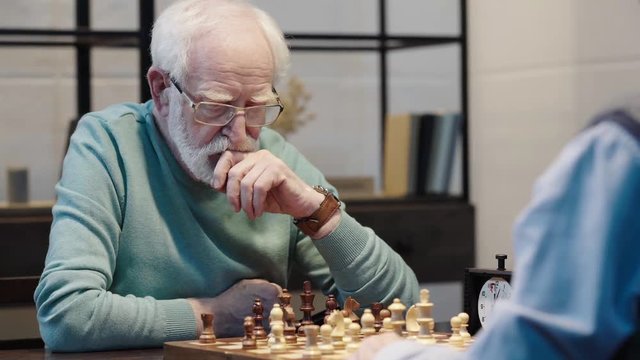 cropped view of two senior men playing chess and pressing button on chess clock