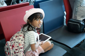 little girl smiling when sitting and hold a tab look at the camera in the airport waiting room