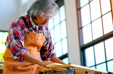 Elder Asian craftsman is working with wood product in the room with day light.