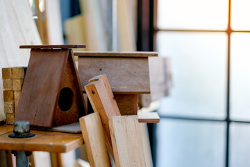Small wood house or bird box are put on the shelves among wood pile and other equipment for crafting in the room.