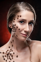 Obraz premium Beautiful smiling girl with naked shoulders. Coffee beans were artistically stuck to the healthy clean skin of her face and neck. Advertising and commercial design. Close up. Copy space