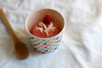 Strawberry vegan ice cream, decorated with raspberry and coconut flakes, in colorful paper cup. Selective focus.