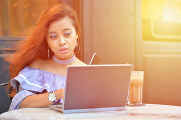 Portrait of successful young woman with laptop in street cafe with sunlight