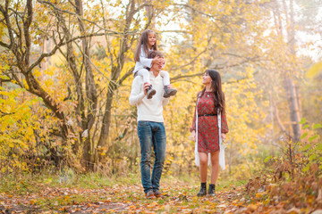 Fototapeta premium Mom, dad and daughter walk through the autumn forest. Daughter sits on father's shoulders