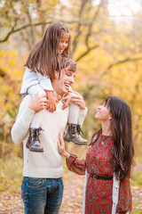 Obraz premium Mom, dad and daughter walk through the autumn forest. Daughter sits on father's shoulders