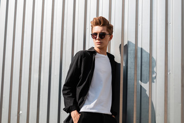 Young cool hipster man with a trendy hairstyle in elegant clothes in fashionable dark sunglasses...