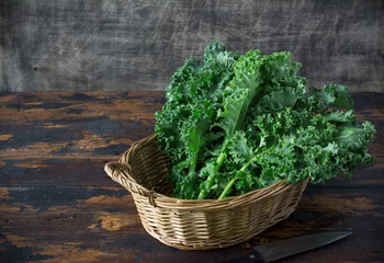 Poster Fresh organic curly kale leaves in a basket with cook knife in a front, on a brown wooden table and on a dark wooden background, gmo free,  rustic style, copy space, horizontal board, free space left © Andrey