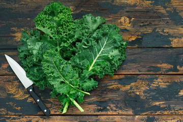 Fresh organic curly kale leaves on a brown wooden table with cook knife, gmo free,  rustic style, free space right side, top view