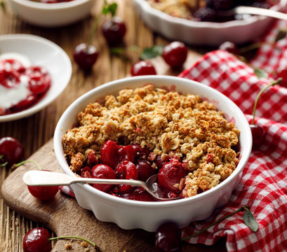 Crumble, cherry crumble, stewed fruits topped with crumble of oatmeal, almond flour, butter and sugar  in a baking dish on a wooden table, close-up